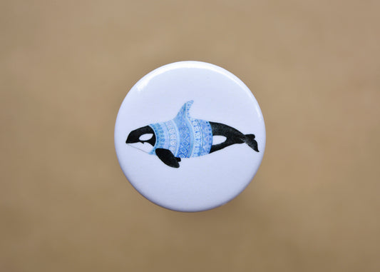 Ink drawing of a humpback whale wearing a blue sweater on a pin-backed button.