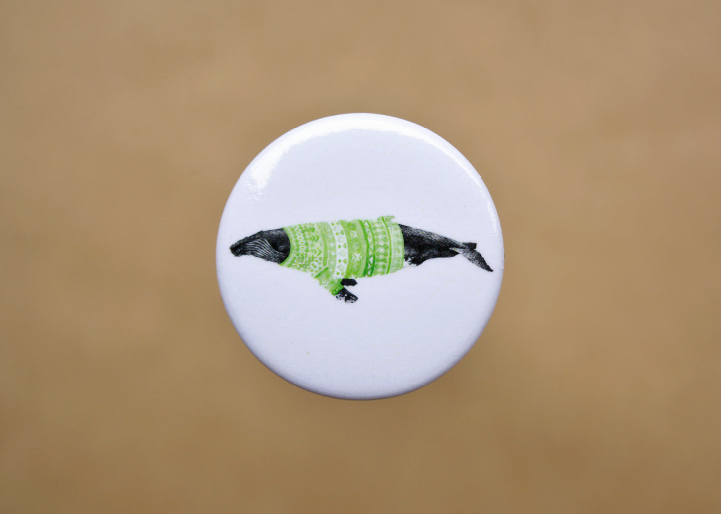 Ink drawing of a humpback whale wearing a green sweater on a pin-backed button.
