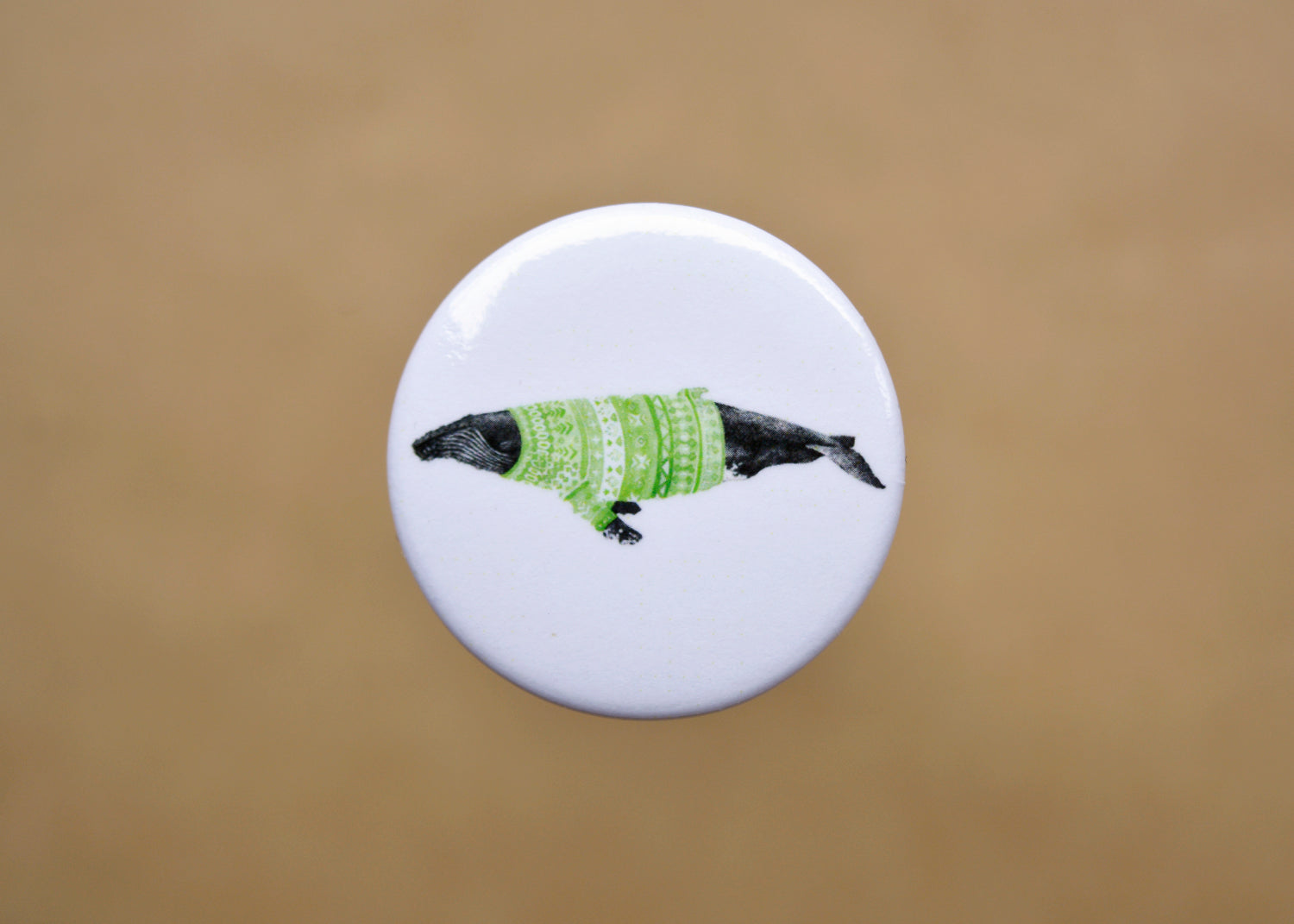 Ink drawing of a humpback whale wearing a green sweater on a pin-backed button.