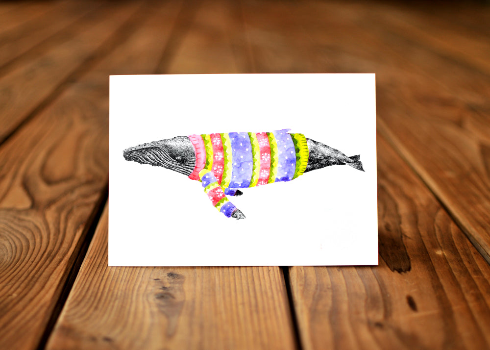 A card with a ink dawing of a humpback whale wearing a colorful sweater.