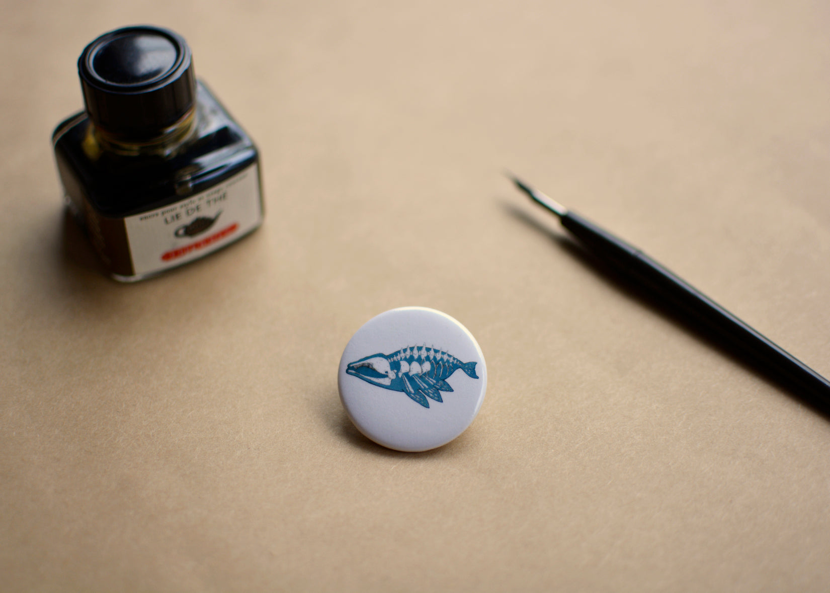 Pin back button with an imaginative skeleton whale. Ink bottle and dip pen featured with the pin.