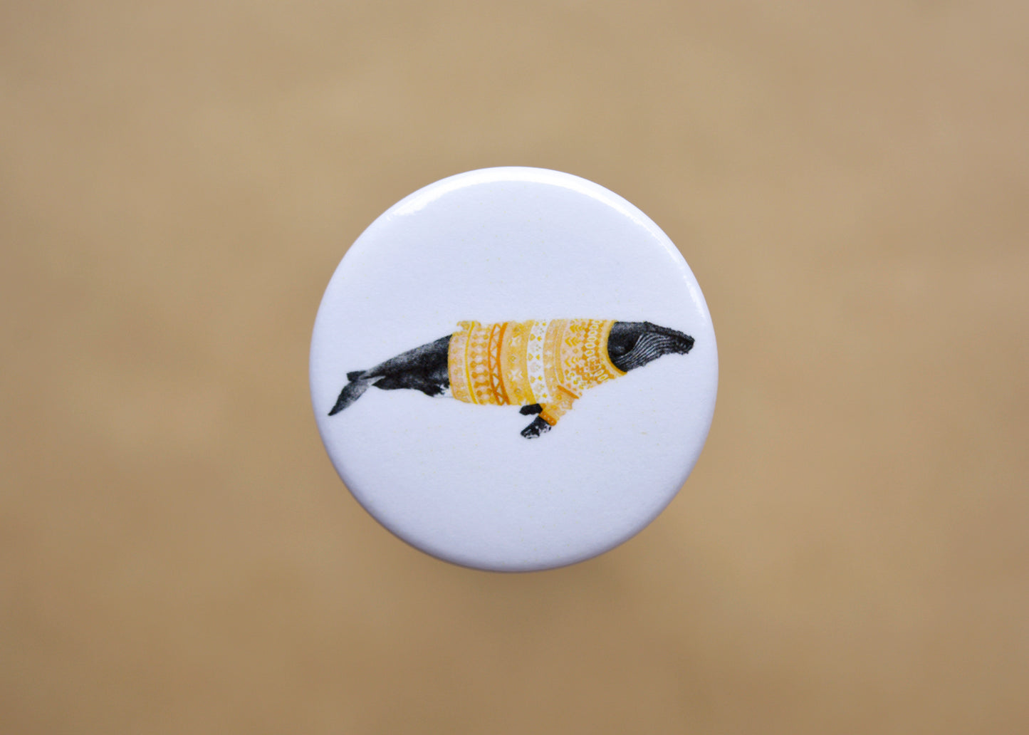 Ink drawing of a humpback whale wearing a orange sweater on a pin-backed button.