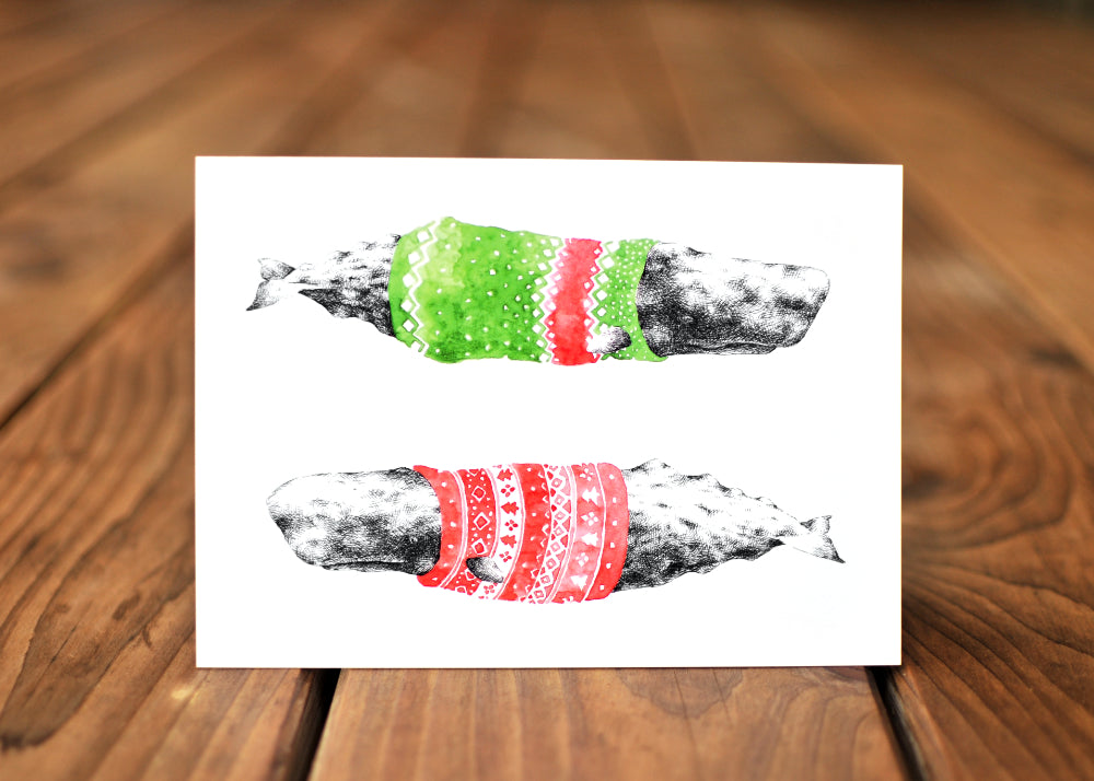 A card with a ink drawing of two sperm whale wearing a colorful sweaters.