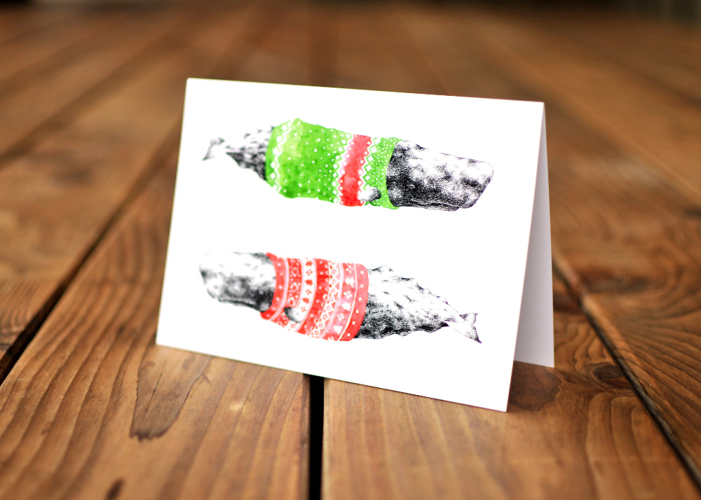 A card with a ink dawing of a humpback whale wearing a colorful sweater.