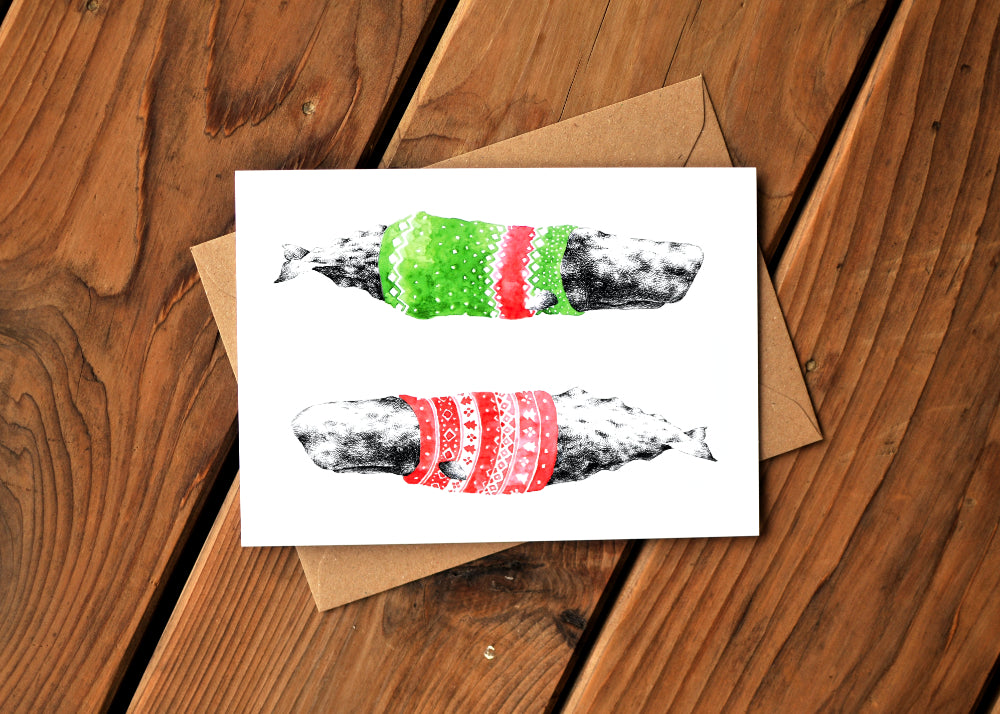 A card with a ink dawing of a humpback whale wearing a colorful sweater. Card is on top of an envelope.