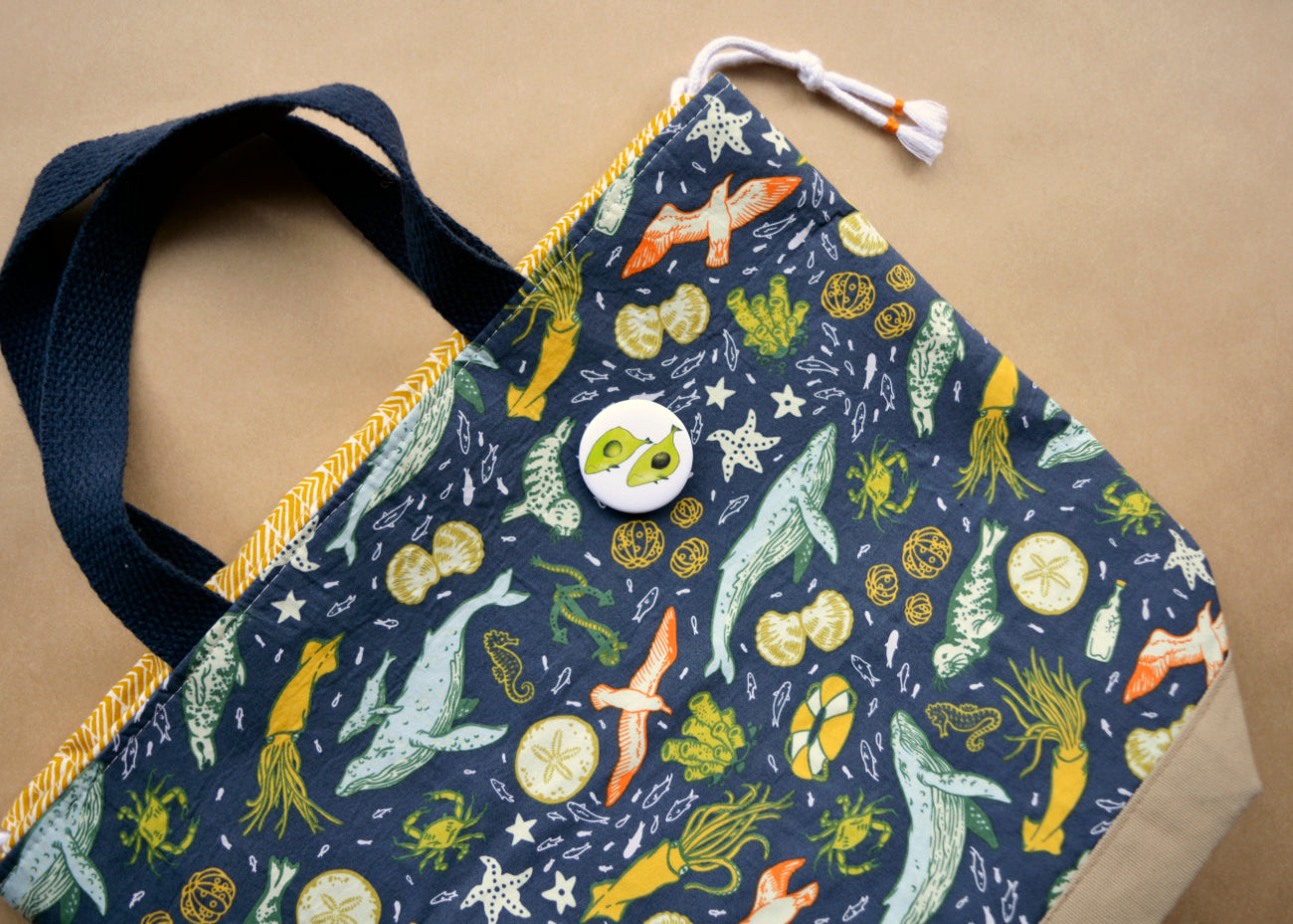 Pin back button with two imaginative "Avocado whales" on a cloth bag.