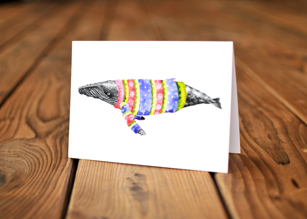 A card with a ink dawing of a humpback whale wearing a colorful sweater.