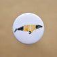 Ink drawing of a humpback whale wearing a orange sweater on a pin-backed button.