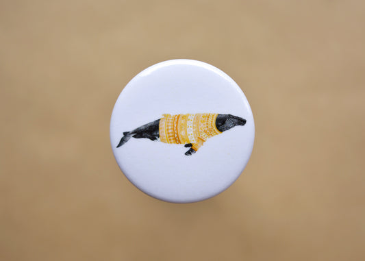 Ink drawing of a humpback whale wearing a orange sweater on a pin-backed button.